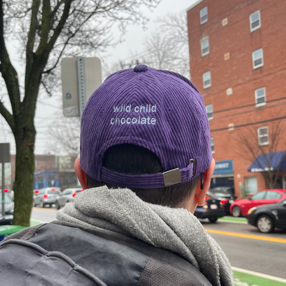 hat on head in city, reads wild child chocolate in blue on purple corduroy hat